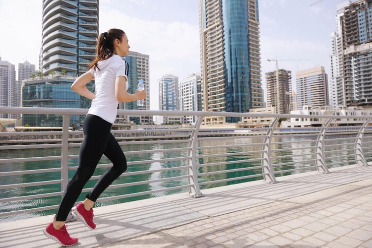 Running in city park. Woman runner outside jogging at morning with Dubai urban scene in background